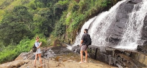 Ein Wasserfall mit zwei Personen auf einer felsigen Klippe.