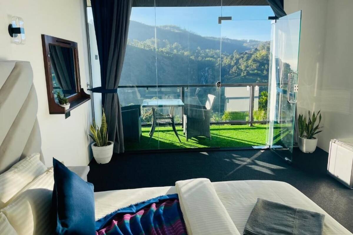 Un dormitorio moderno con una cama grande, una puerta de vidrio que da a un balcón con vistas a un paisaje verde y montañas.