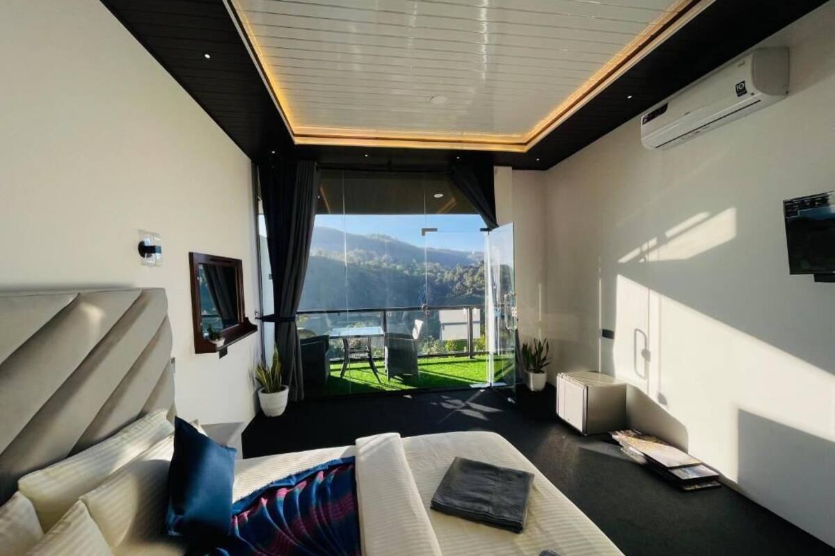 Un dormitorio moderno con cama, televisor y balcón con vistas a zonas verdes y colinas.