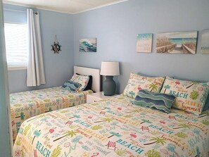 Ein Schlafzimmer mit zwei Betten, einem Nachttisch, einer Lampe und Wandbildern zum Thema Strand.