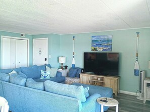 Ein Wohnzimmer mit blauem Sofa, einem Flachbildfernseher und einem Gemälde eines Segelboots.