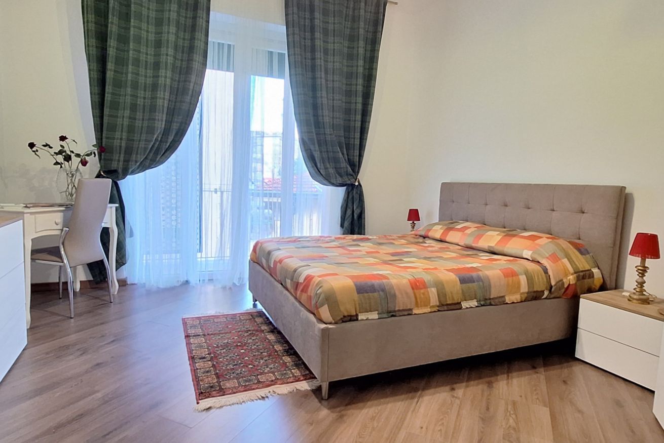 Un dormitorio con cama, escritorio, silla, mesita de noche y ventana con cortinas.