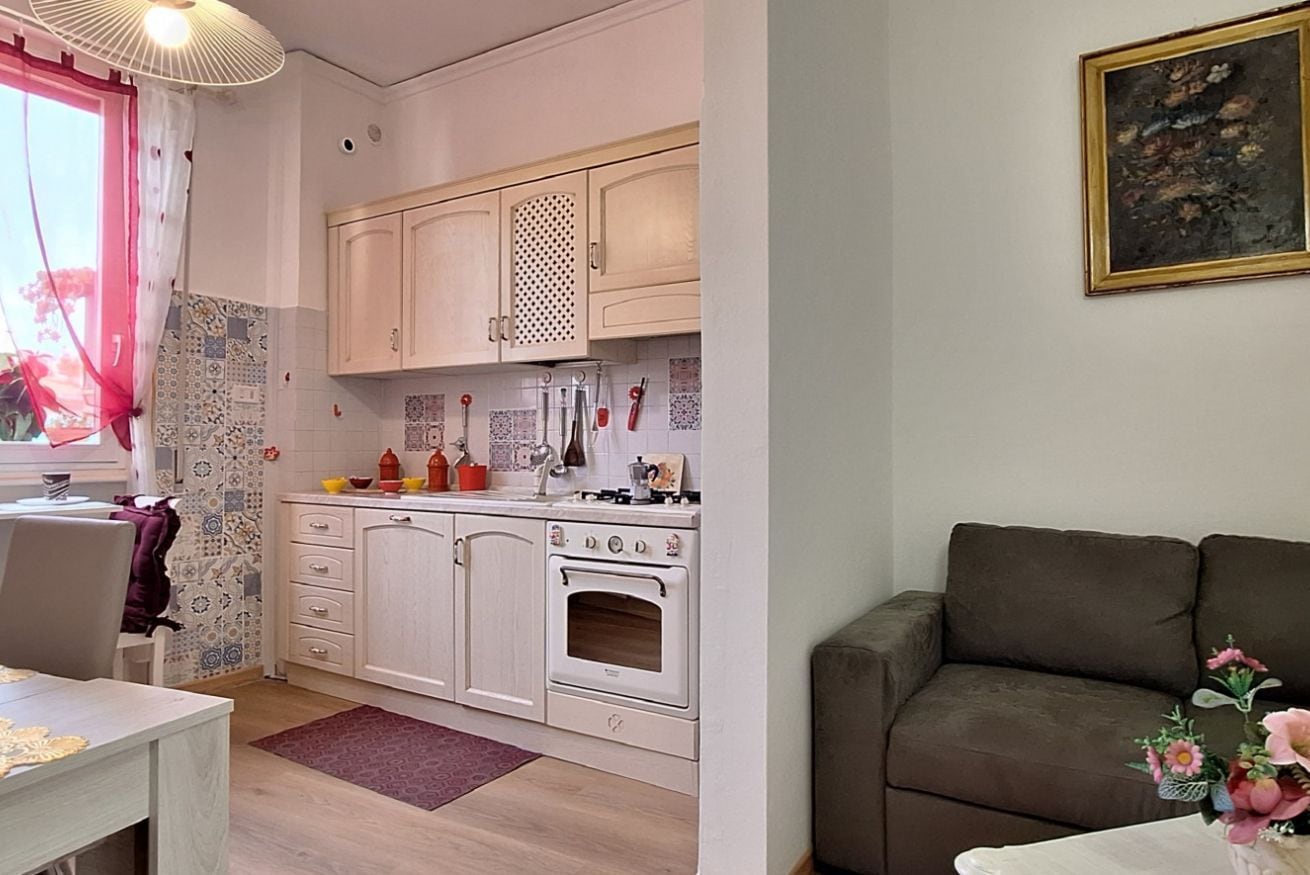 Cocina compacta con armarios blancos, estufa y comedor con mesa y sillas.