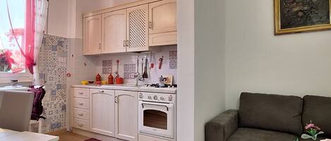 Cocina compacta con armarios blancos, estufa y comedor con mesa y sillas.