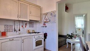 A kitchen with white cabinets, a stove, and a sink. There is a small table with a plant and a chair. - Casa Puccini - Cozy 2-bedroom Florentine home (Florence)