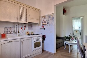 A kitchen with white cabinets, a stove, and a sink. There is a small table with a plant and a chair. - Casa Puccini - Cozy 2-bedroom Florentine home (Florence)