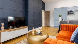 A modern living room with a flat-screen TV, a round gold coffee table, and an orange sofa.