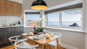 A modern kitchen with a dining area, large windows with a view, and a pendant light.