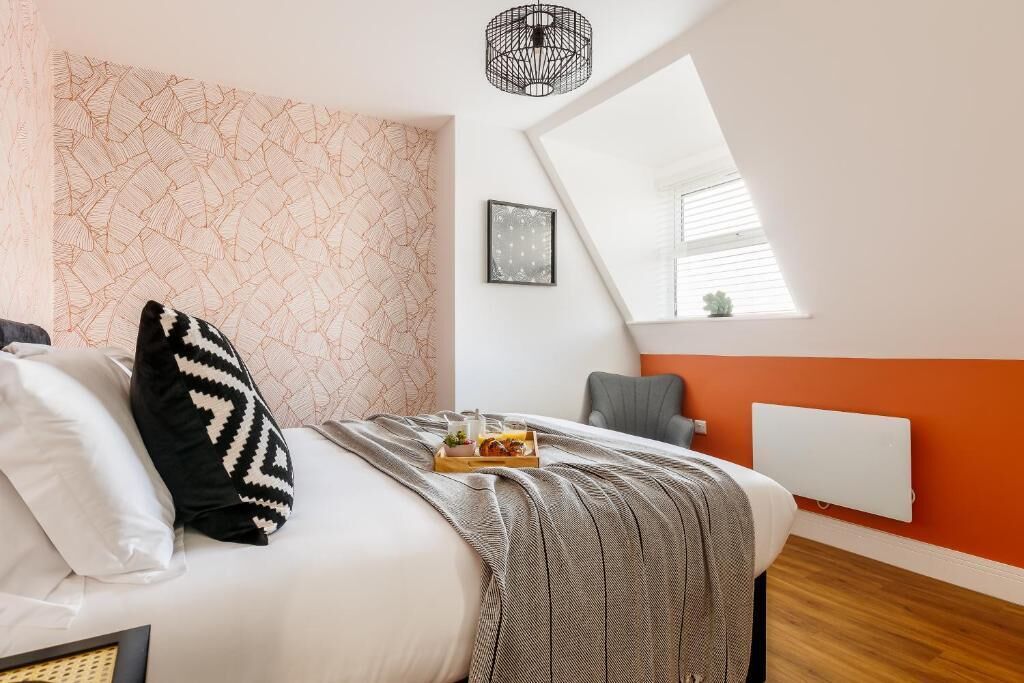 Slaapkamer met een bed, kussens, een dienblad met eten, een stoel, een radiator en een raam met jaloezieën.