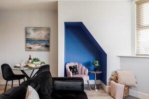 Una sala de estar moderna con comedor, una pared azul como acento, un sillón rosa y una pequeña mesa con una planta.