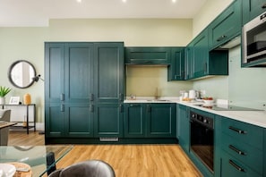 Una cocina moderna con armarios azul turquesa, un horno de acero inoxidable y una mesa de comedor de vidrio.