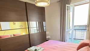 Una camera da letto con un letto, un comodino, uno specchio, una lampada a sospensione e vista sull'esterno.