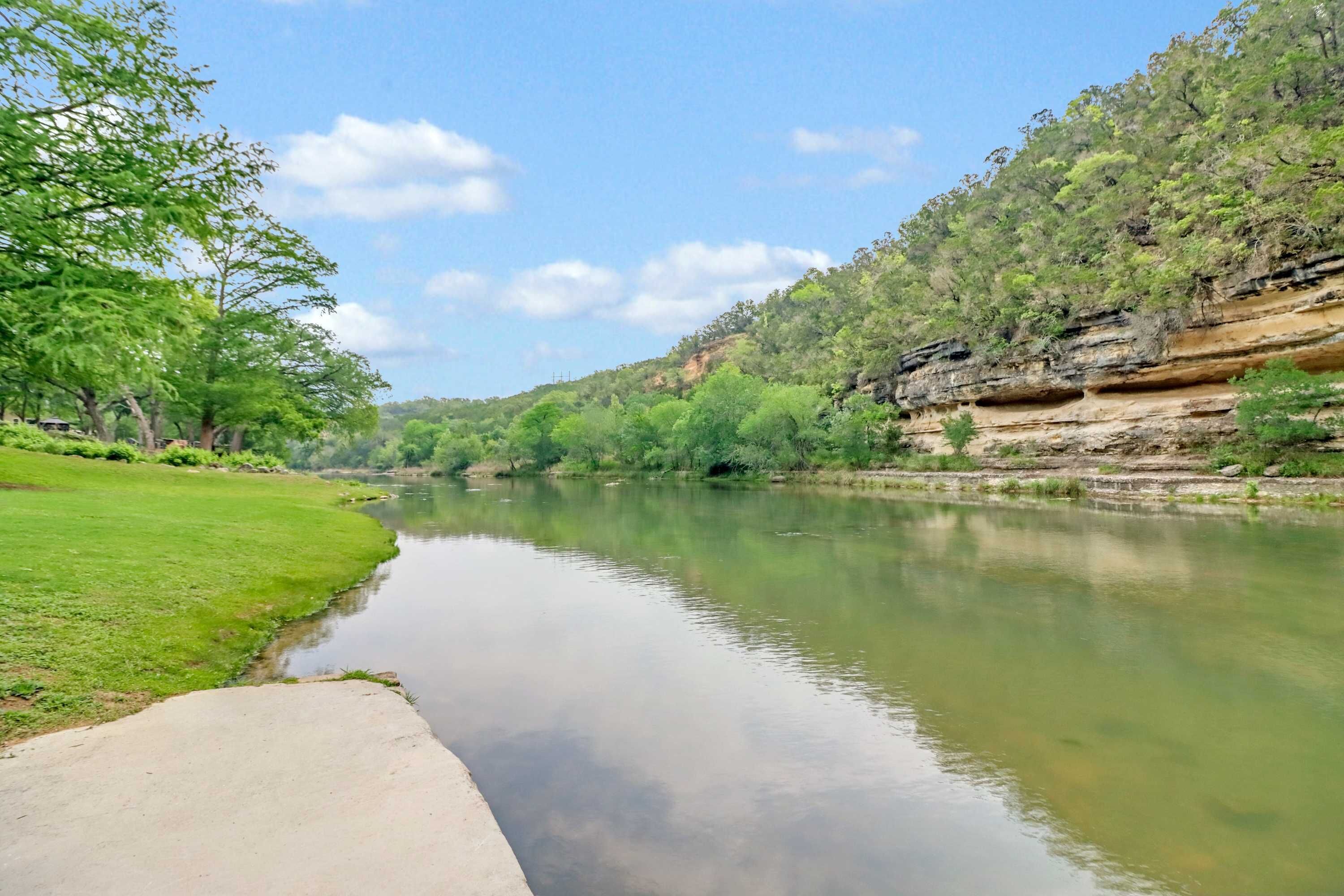 A river with a concrete path alongside, surrounded by greenery and trees.