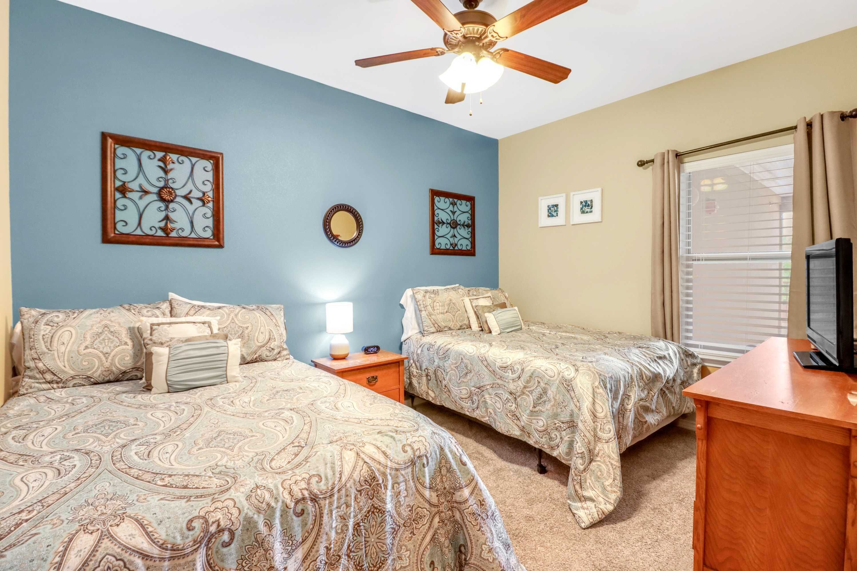 A bedroom with two beds, a ceiling fan, a TV, and a window with curtains.