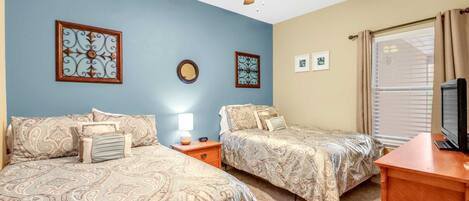 A bedroom with two beds, a ceiling fan, a TV, and a window with curtains.
