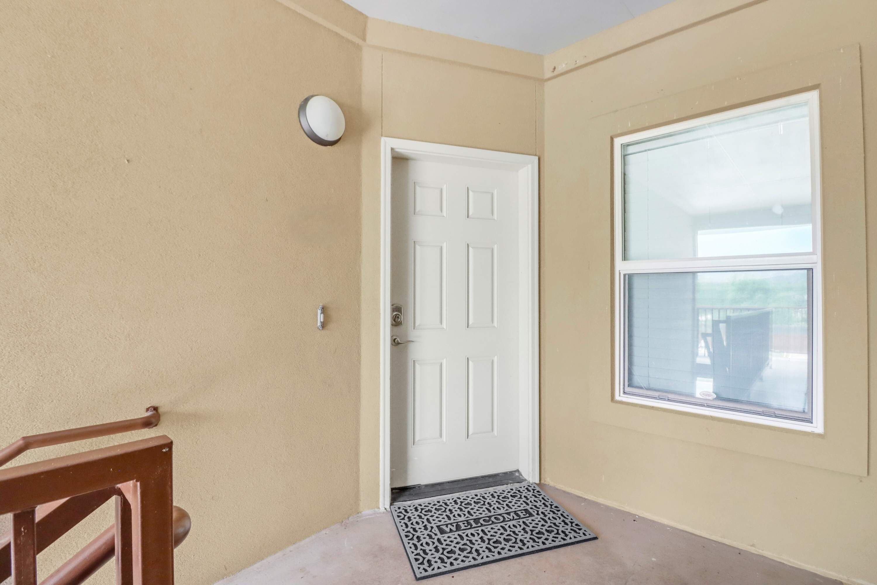 A hallway with a white door, a window, and a welcome mat.