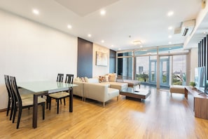 A modern living room with a glass dining table, sofas, and a large window offering a city view. - TRACY SAILING TOWER (Ho Chi Minh)