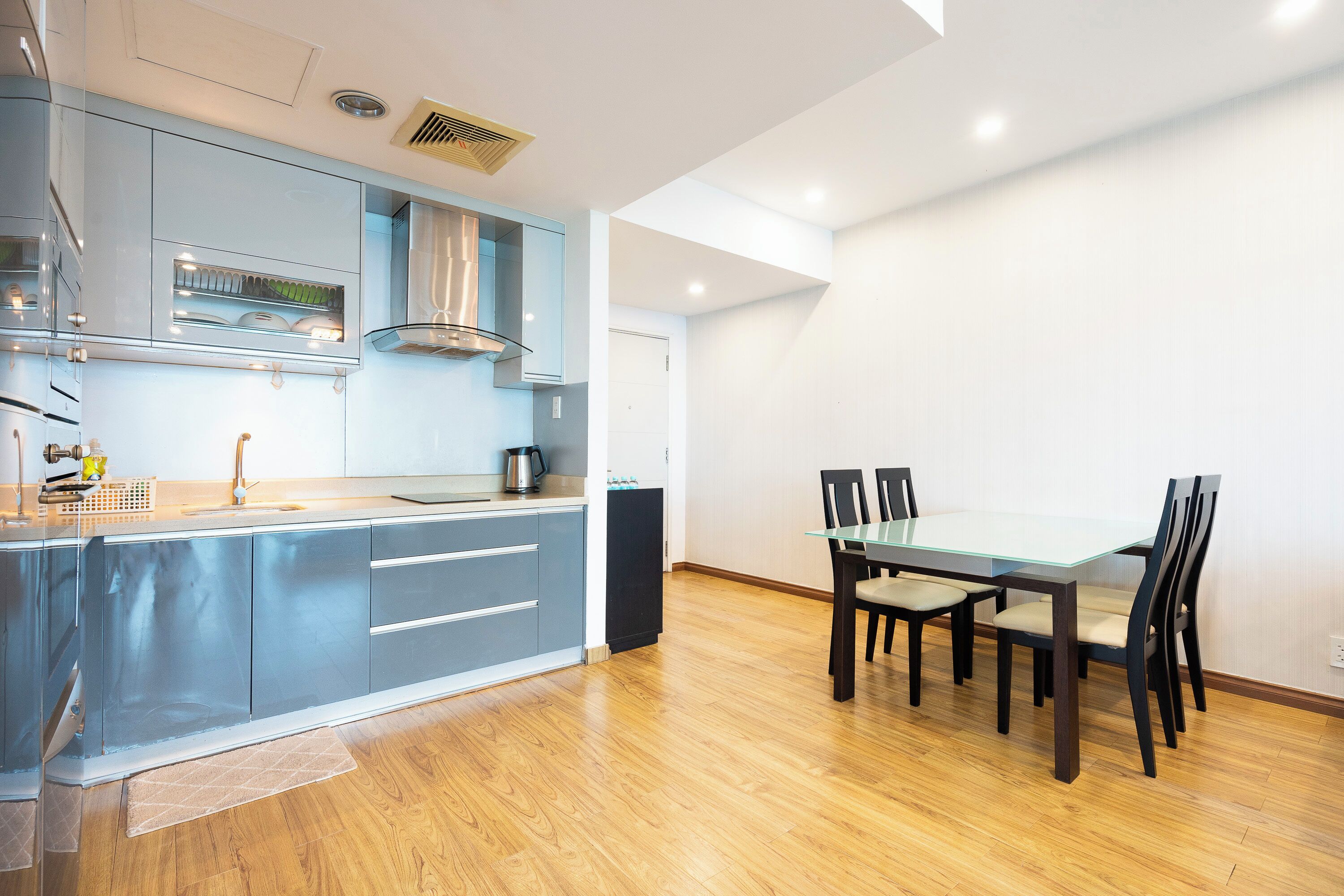 A modern kitchen with a dining area, wooden flooring, and a glass table.