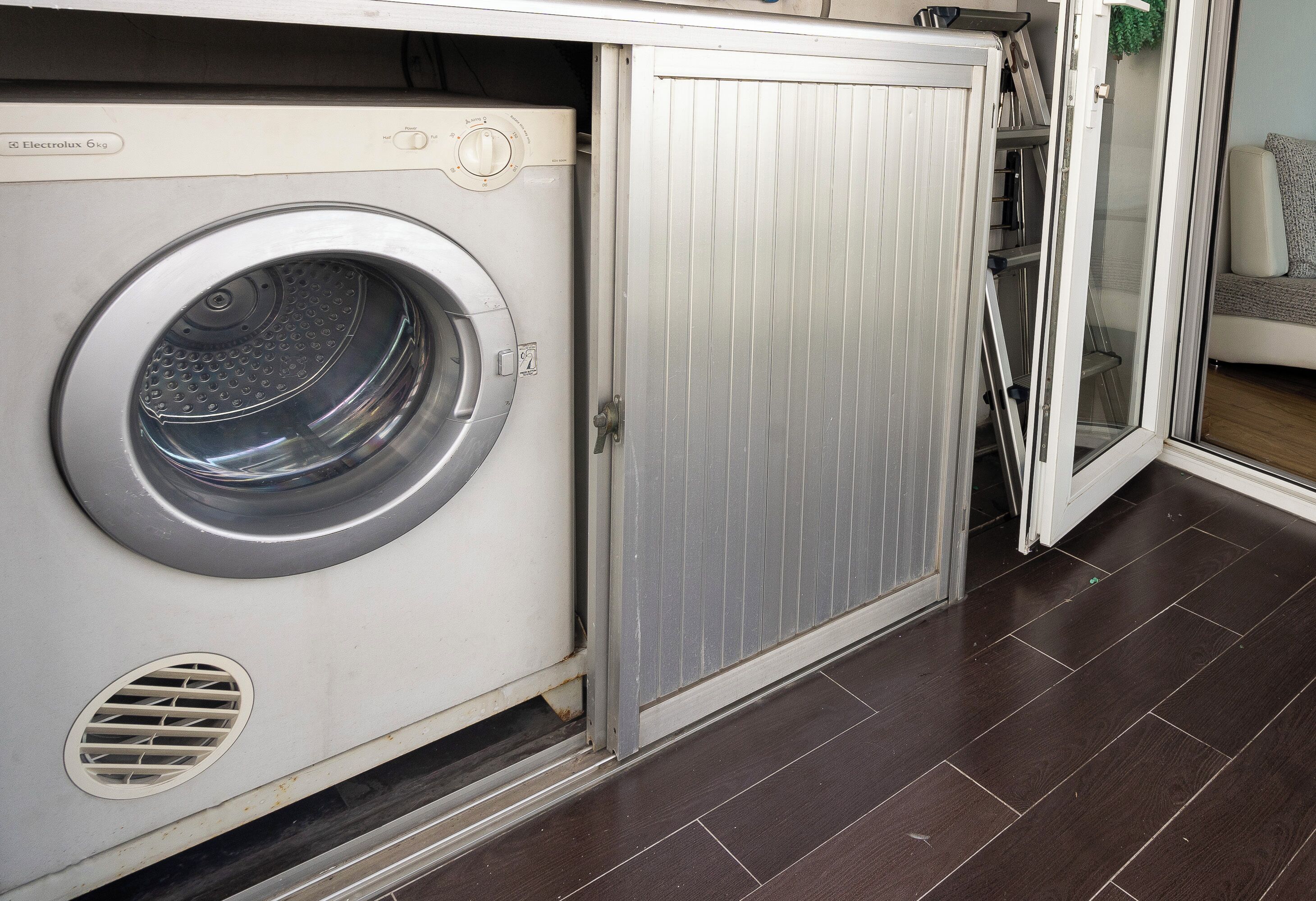 A compact, modern laundry room with a front-loading washing machine, a metal cabinet, and a sliding glass door leading to a living area.