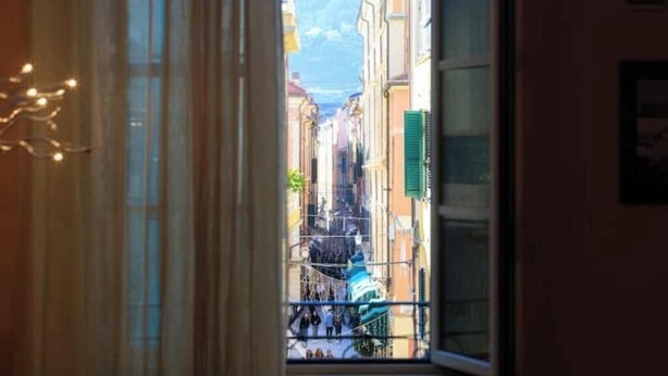 Vista a través de una ventana de una calle estrecha con edificios y una montaña al fondo.