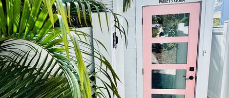 A white building with a pink door, labeled 'Paisley's Casa,' and a black outdoor light fixture above it.