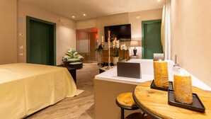 A hotel room with a bed, a desk with a laptop, a small table with candles, and a TV on the wall. - B&B Relax Assoluto - Luxury Urban Spa (Casalbordino)