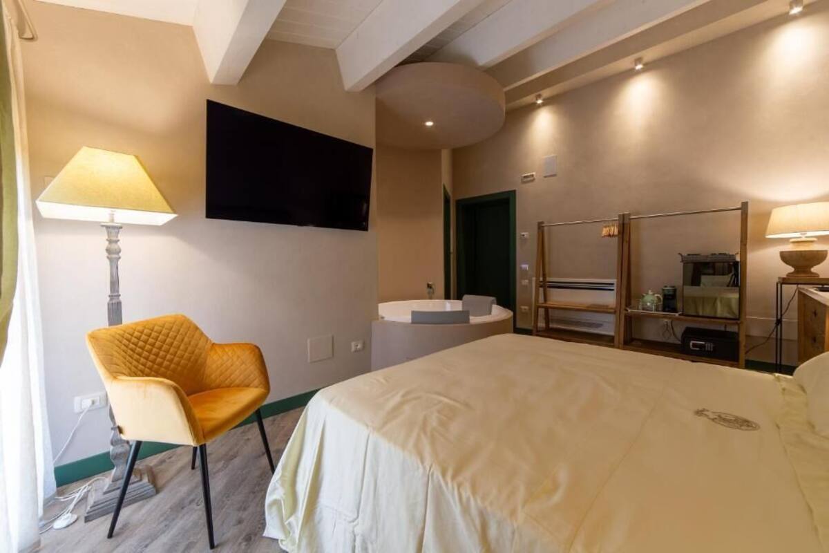 A hotel room with a bed, a chair, a TV, a bathroom with a sink and mirror, and a wardrobe.