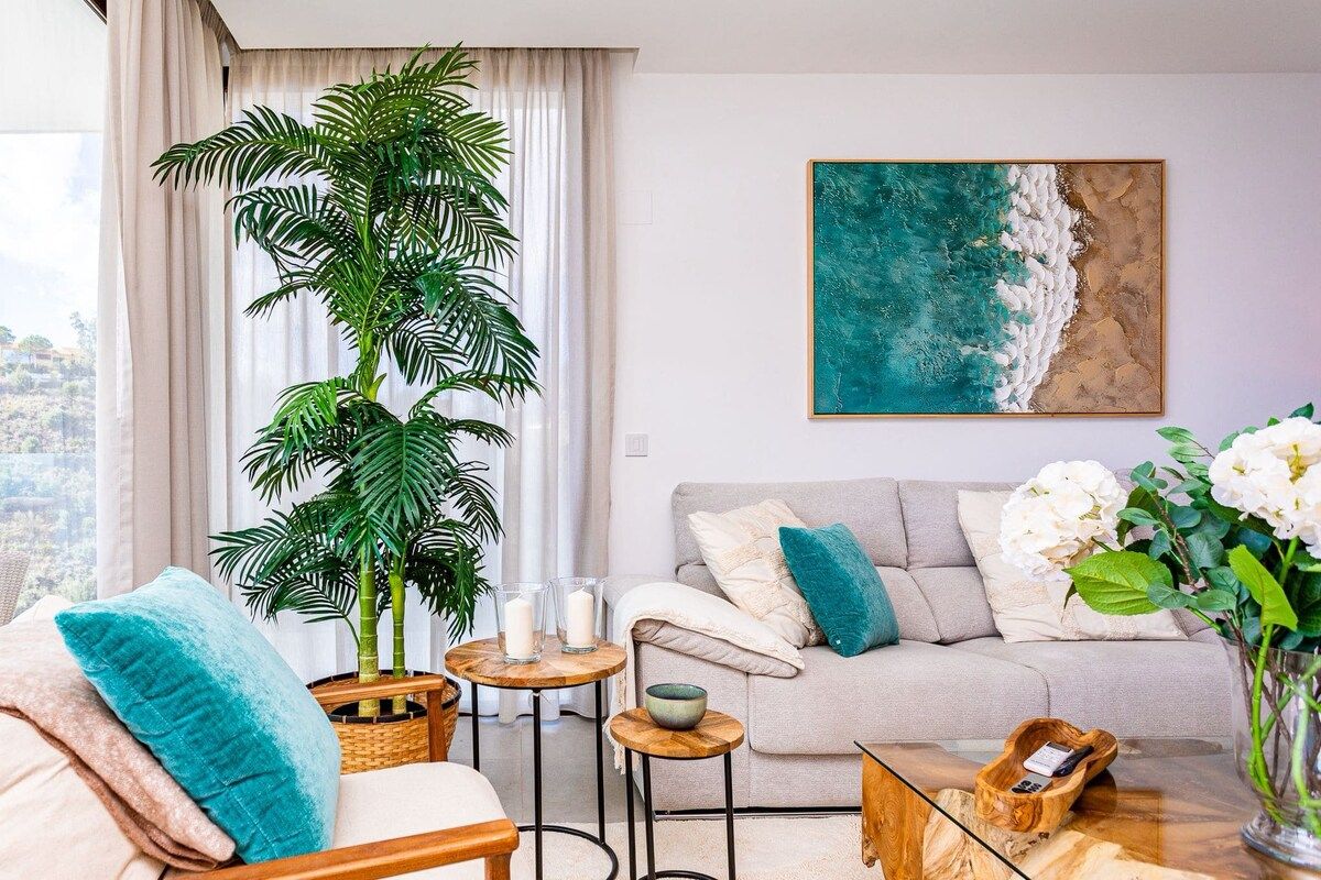 A living room with a sofa, a coffee table, a plant, and a painting of a beach scene.