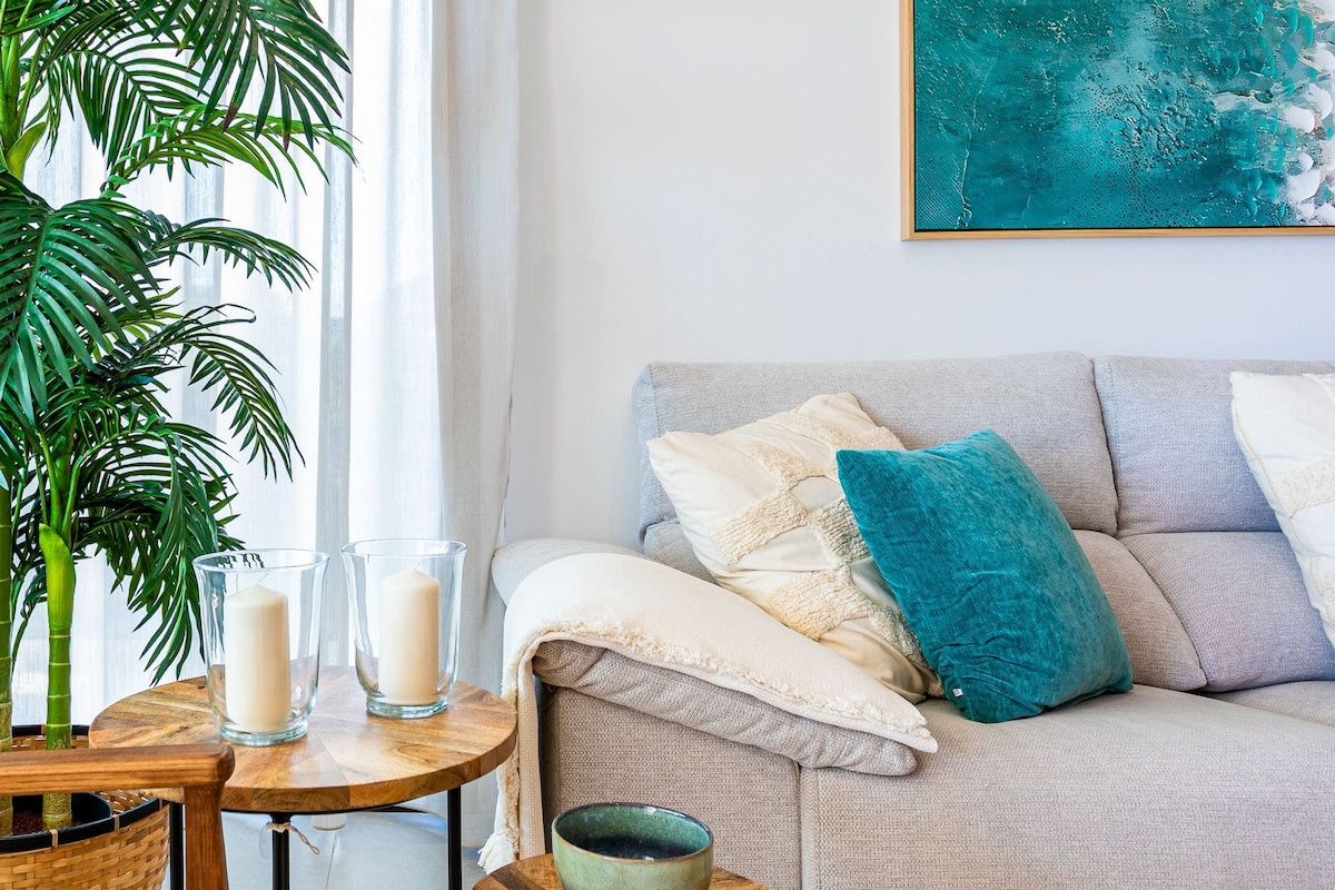 A living room with a sofa, a table with candles, a potted plant, and a painting on the wall.