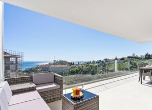 Ein Balkon mit Blick auf das Meer und die Stadtlandschaft, ausgestattet mit einer Couch und einem Tisch mit Obst.