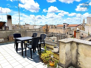 Une terrasse sur le toit, avec une table et des chaises, des plantes en pot et une vue sur le paysage urbain.