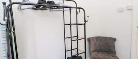 Uma cama beliche com estrutura de metal, uma poltrona estofada cinza e um pequeno banquinho.