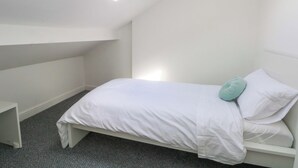 Habitación pequeña, blanca, con una cama individual, techo inclinado y tragaluz.