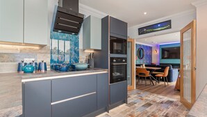 Una cocina moderna con horno empotrado, zona de comedor con mesa redonda y sillas, y televisor montado en la pared.