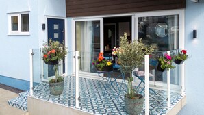 Un edificio con fachada azul, una puerta blanca y una zona de entrada con baldosas y plantas en macetas.