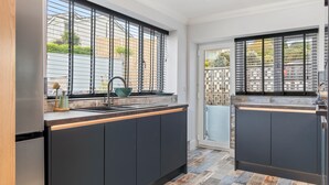 Una cocina moderna con armarios oscuros, un refrigerador de acero inoxidable y una ventana con persianas metálicas.