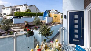 Una propiedad residencial con puerta azul, un pequeño jardín con flores y cerca blanca.