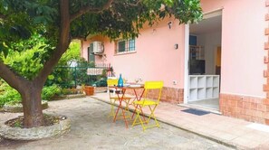 Un bâtiment à la façade rose, un arbre au premier plan et une table avec des chaises à l’extérieur.