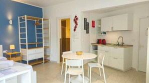 Una stanza compatta con un letto a castello, un piccolo tavolo da pranzo con sedie, angolo cottura e un armadio bianco.
