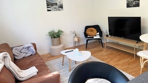 A living room with a brown sofa, a black chair, a white coffee table, a TV, and two wall-mounted pictures. - 2 Bedroom Condo With Cheap Pick up Services (Reykjavik)