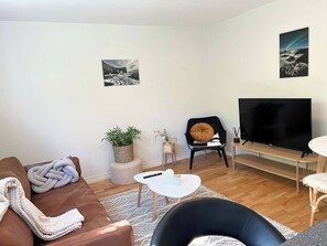 Ein Wohnzimmer mit braunem Sofa, einem schwarzen Sessel, einem weißen Couchtisch, einem Fernseher und zwei an der Wand befestigten Bildern.