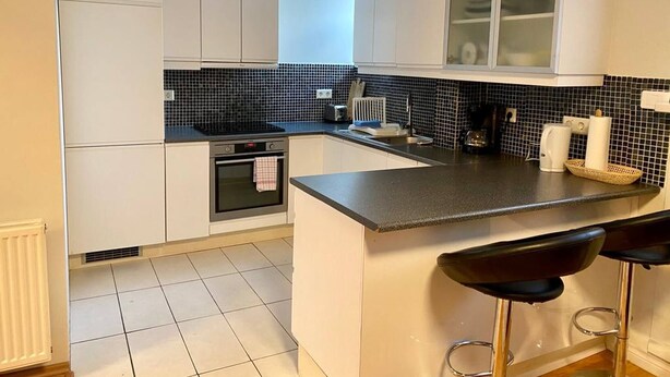 A modern kitchen with white cabinets, a black countertop, and a small island with bar stools. - 2 Bedroom Condo With Cheap Pick up Services (Reykjavik)