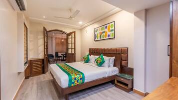 A hotel room with a bed, a desk, a chair, a wardrobe, and a ceiling fan.