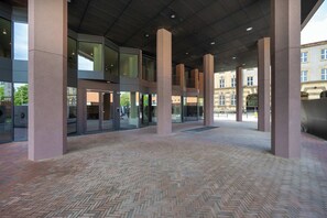 A covered outdoor area with a herringbone-patterned brick floor, large pillars, and glass doors leading to a building. - Luxury Apartment with Parking | Air Conditioning | Near the Market Square (Wrocław)