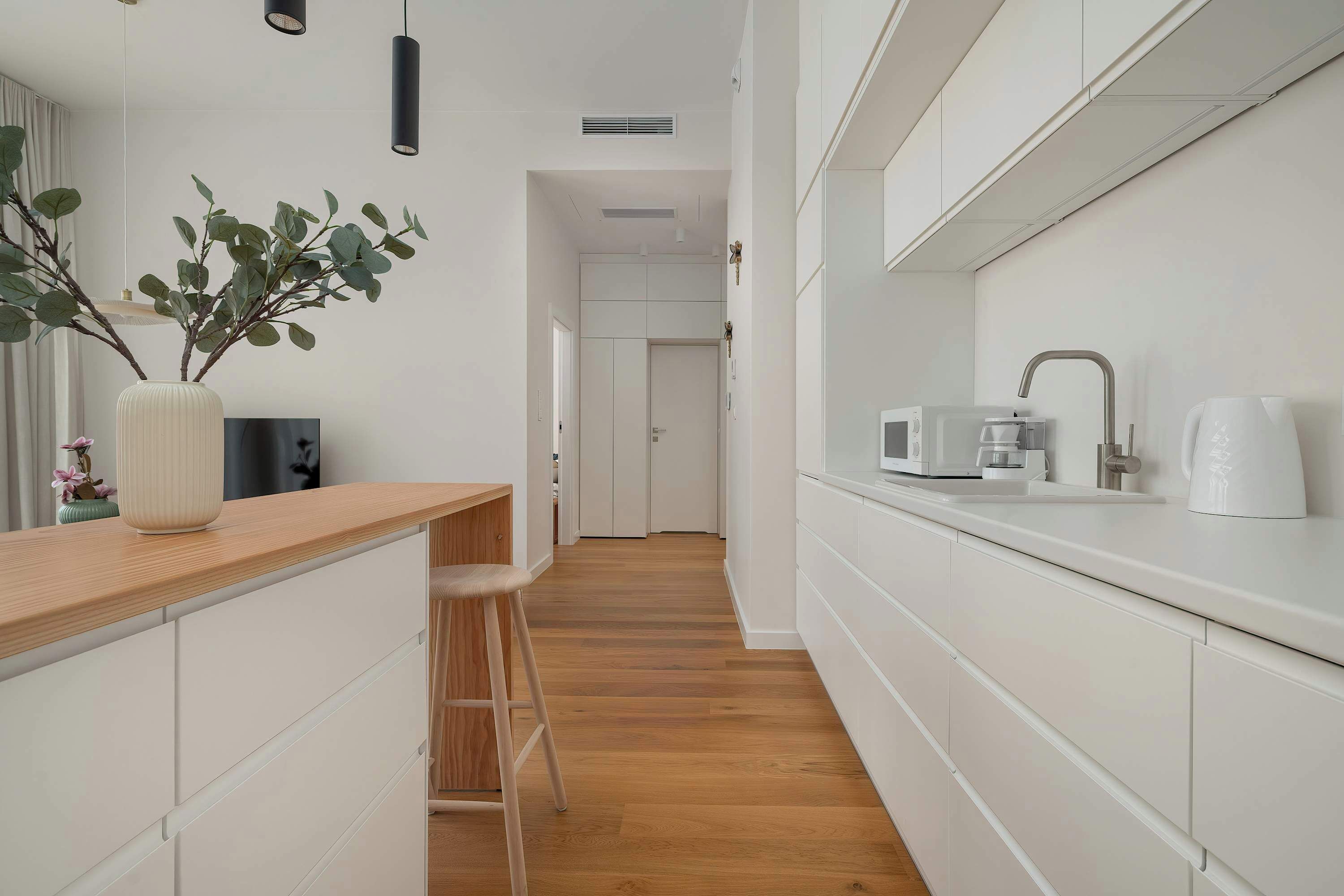 Une cuisine moderne avec des meubles blancs, un plan de travail en bois, un tabouret de bar et une plante en pot.