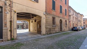 A cobblestone street with a building featuring an arched entrance and a brick facade. - GuestHost - Bright Apartment with Patio & Parking (Ferrara)
