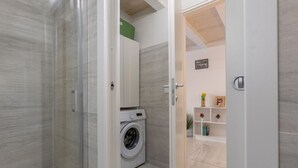 A modern bathroom with a glass shower enclosure, a built-in washing machine, and a vanity with a mirror. - GuestHost - Bright Apartment with Patio & Parking (Ferrara)