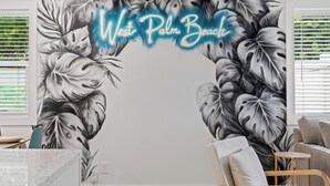 Un mural en la pared con un diseño de hojas tropicales y el texto 'West Palm Beach' en estilo de letrero de neón.