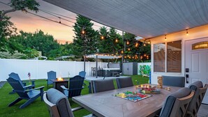 Un patio trasero con mesa y sillas de madera, y un hogar para fuego.