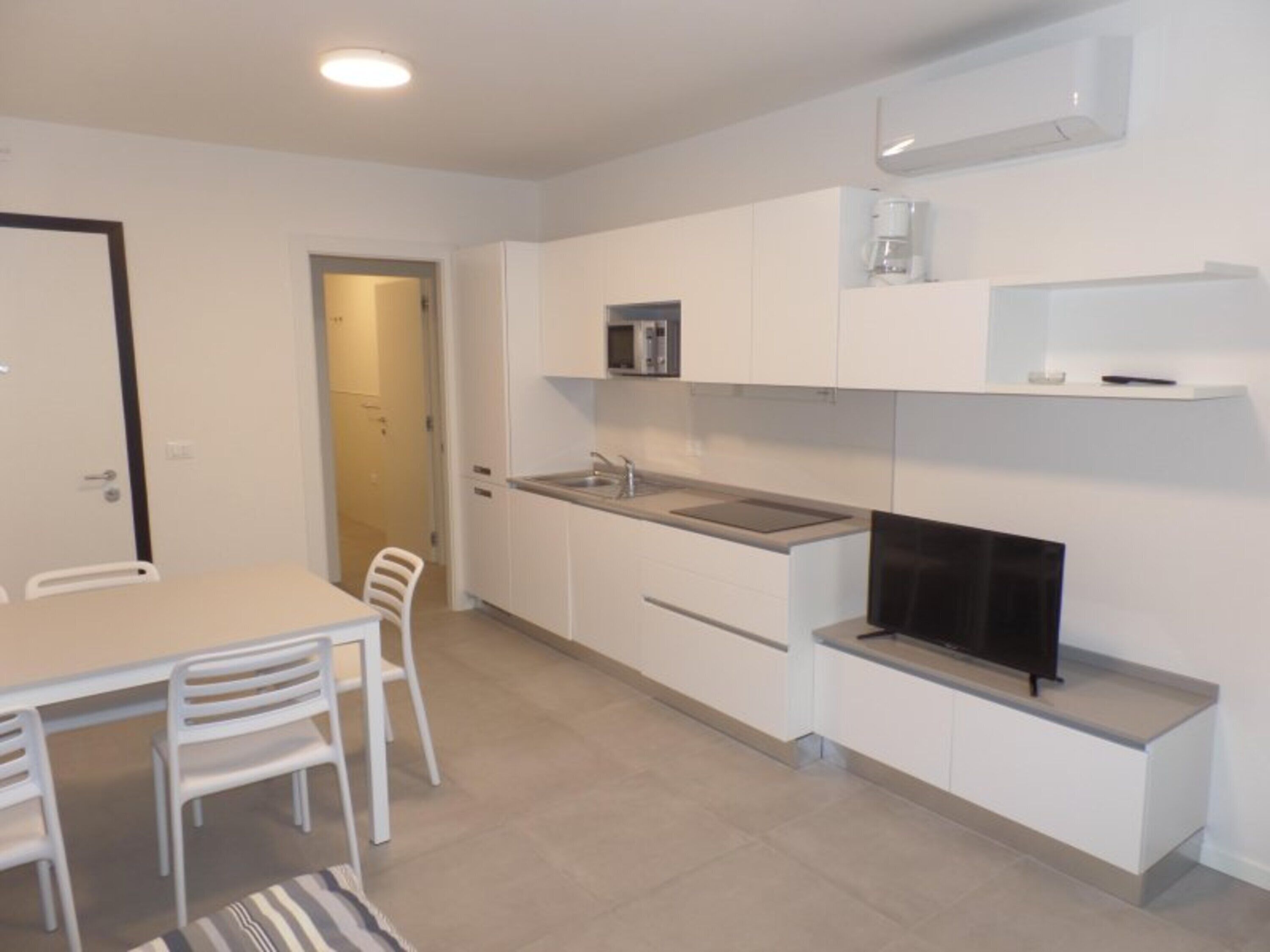 Una cocina moderna con armarios blancos, una estufa empotrada y un televisor de pantalla plana.